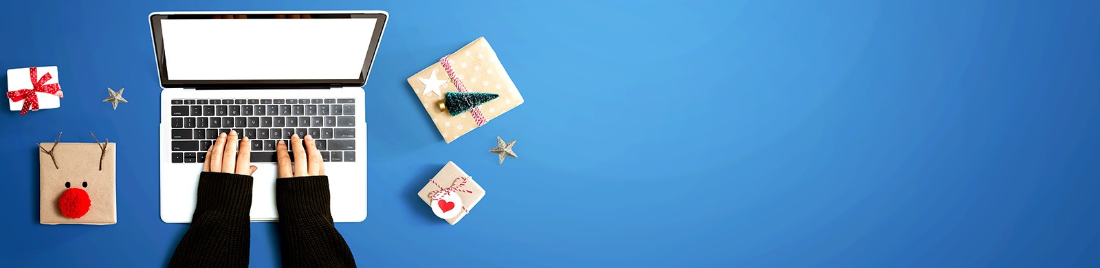 blue background photo of white laptop with hands, black sweater, four holiday presents