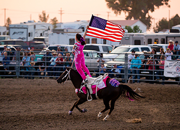 photo of a girl riding on top of a horse carrying an American flag