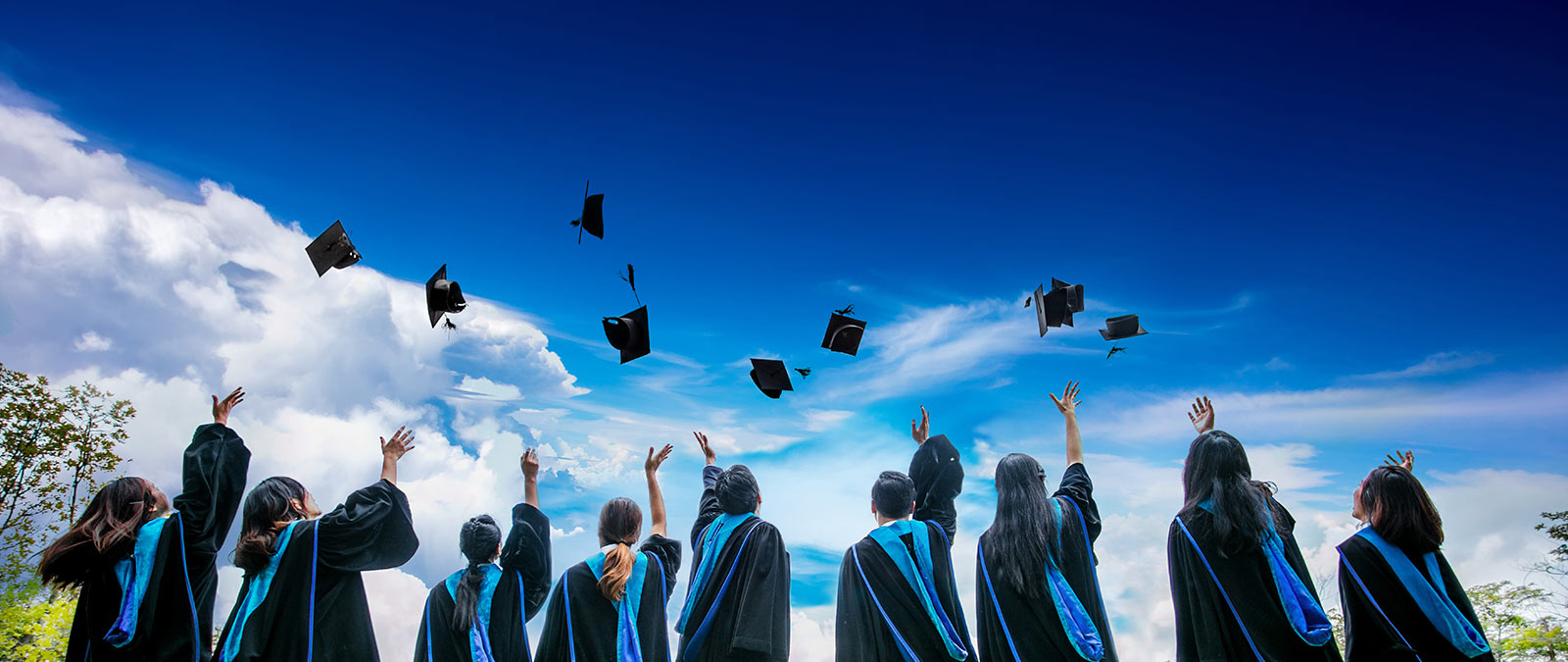 Photo of graduates tossing hats into the air with clouds and a blue sky