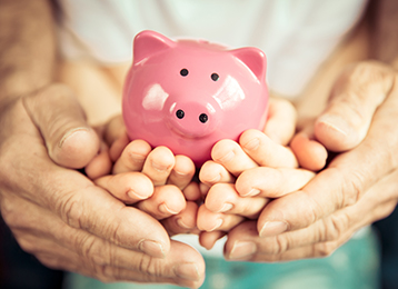 photo of three pairs of hands holding a pink piggy bank