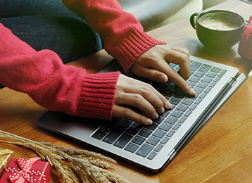 Photo of woman's hands on a laptop keyboard with a coffee mug, gifts, and wheat