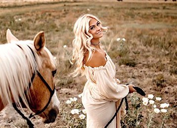 photo of a Caucasian woman with blond hair with a horse in a field with daisies