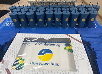 Sheet cake with high Plains Bank logo on a blue table cloth with blue and yellow cups